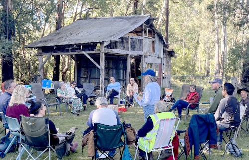 Group sitting outside in a circle in camp chairs with an old wooden building in the background.