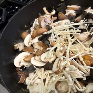 Several kinds of raw mushrooms in a frying pan ready to be cooked.