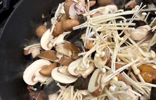 Several kinds of raw mushrooms in a frying pan ready to be cooked.