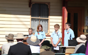 Children on a building porch performing for a seated audience.