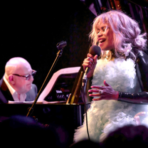 Man sitting at a piano with a vocalist on the right.
