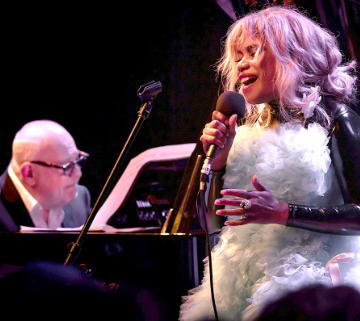 Man sitting at a piano with a vocalist on the right.