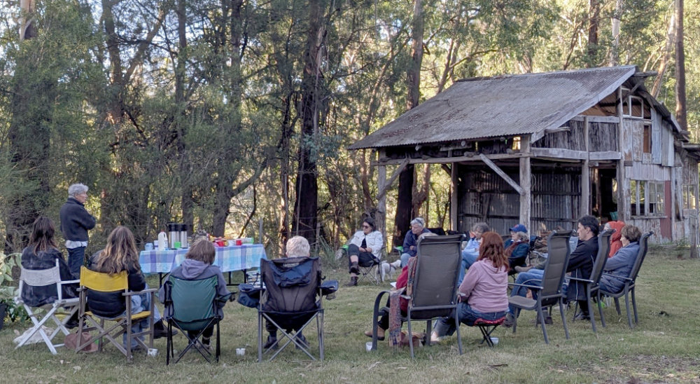 People sitting outside with a wooden building in the background.