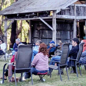 People sitting in a circle outside with an old wooden building in the background