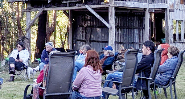 People sitting in a circle outside with an old wooden building in the background