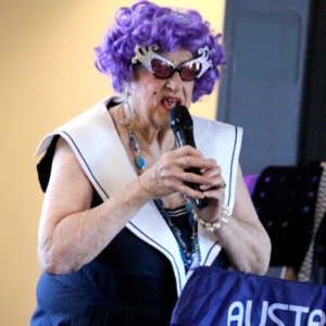 Woman holding microphone in Dame Edna costume