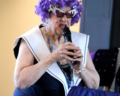Woman holding microphone in Dame Edna costume