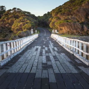 Looking down a one-lane wooden bridge with white side railings.