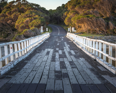 Looking down a one-lane wooden bridge with white side railings.