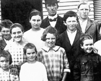 Black and white class photo with teacher wearing a bowler hat in the back row.