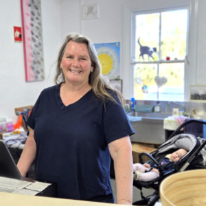 Woman at the counter of an op shop with a baby in a pram in the background