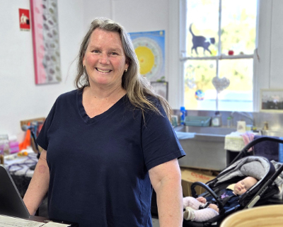 Woman at the counter of an op shop with a baby in a pram in the background