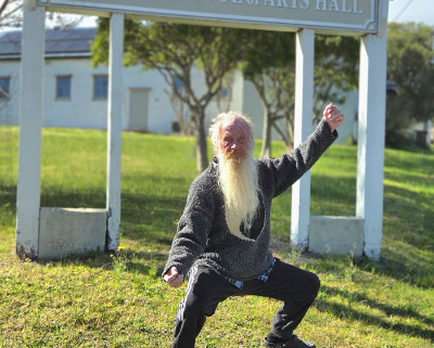 Man in a tai chi pose in front of a sign that says Cobargo School of Arts Hall