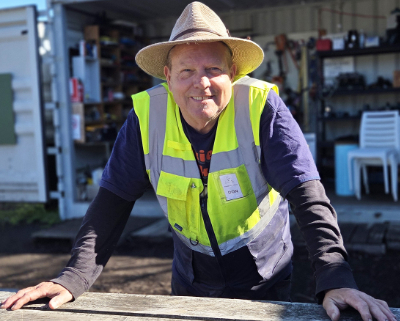 Man in a hat in front of a tool shed