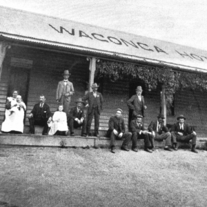 Black and white image of people on the verandah of with the words Wagonga Ho[tel] on the roof.