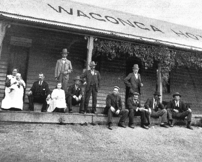 Black and white image of people on the verandah of with the words Wagonga Ho[tel] on the roof.