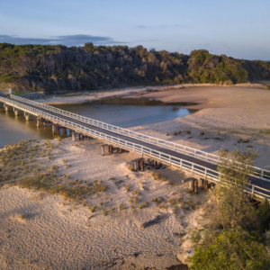 View from the air of a one-lane bridge crossing a sandy estuary.