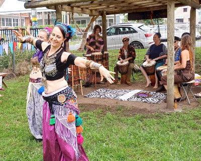 Woman belly dancing with a group of drummers in the background.