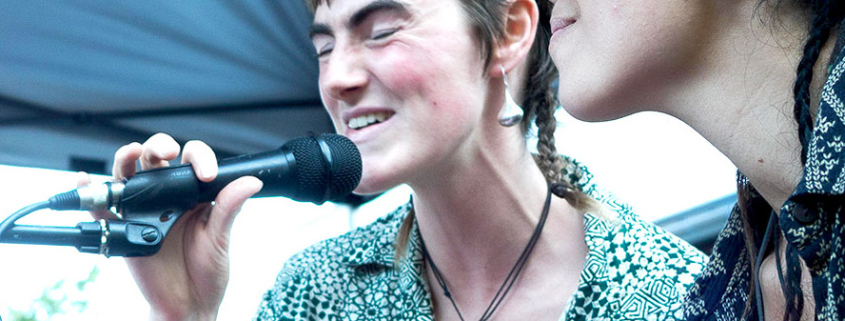 Two women singing at a microphone.