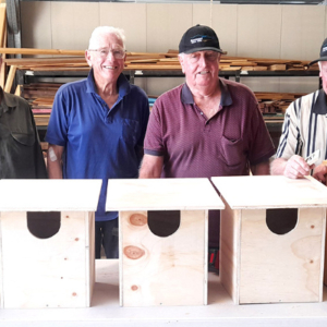 Four men standing behind a table with newly made possum boxes