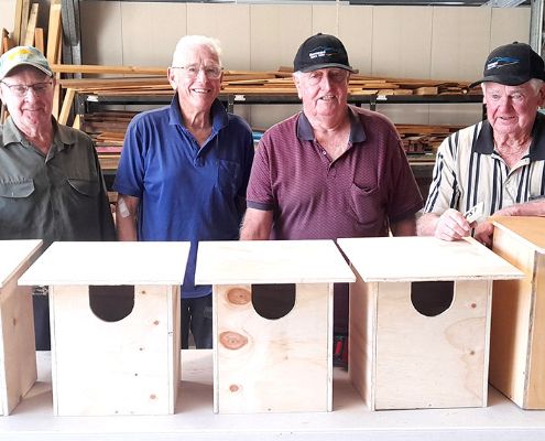 Four men standing behind a table with newly made possum boxes