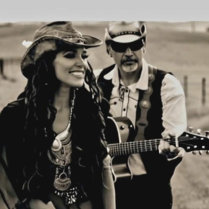 Woman and man in western clothing, the man holding a guitar.