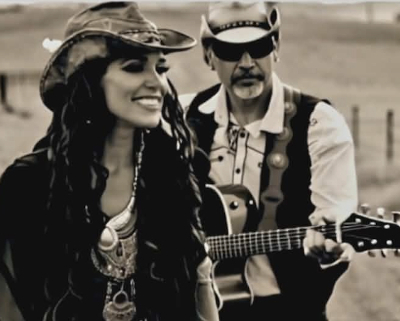 Woman and man in western clothing, the man holding a guitar.