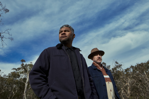 Two men photographed against a dramatic background of cloud streaked sky.