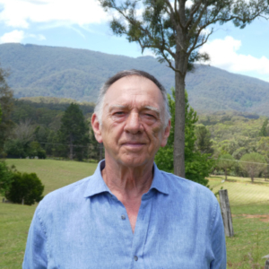 Man in a grassy paddock with a mountain in the background.