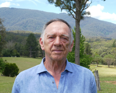 Man in a grassy paddock with a mountain in the background.
