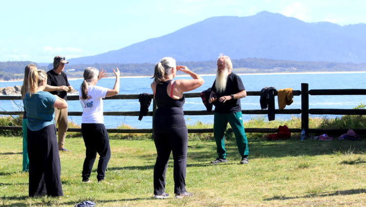 People doing Tai Chi with a mountain across the bay in the background.